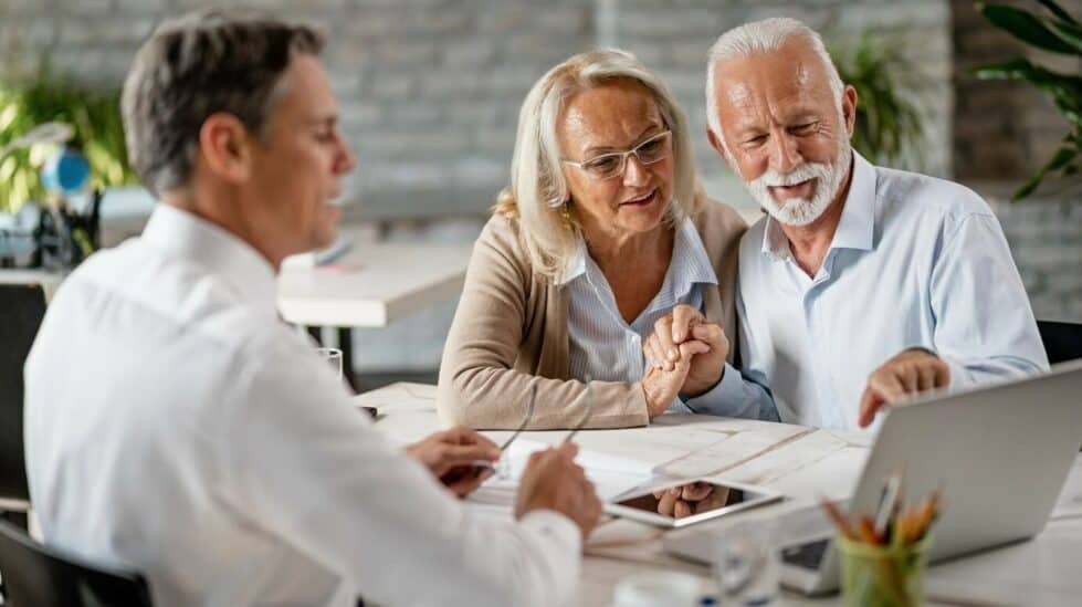 couple de seniors en rendez-vous avec un professionnel. Ils regardent l'ordinateur en souriant.